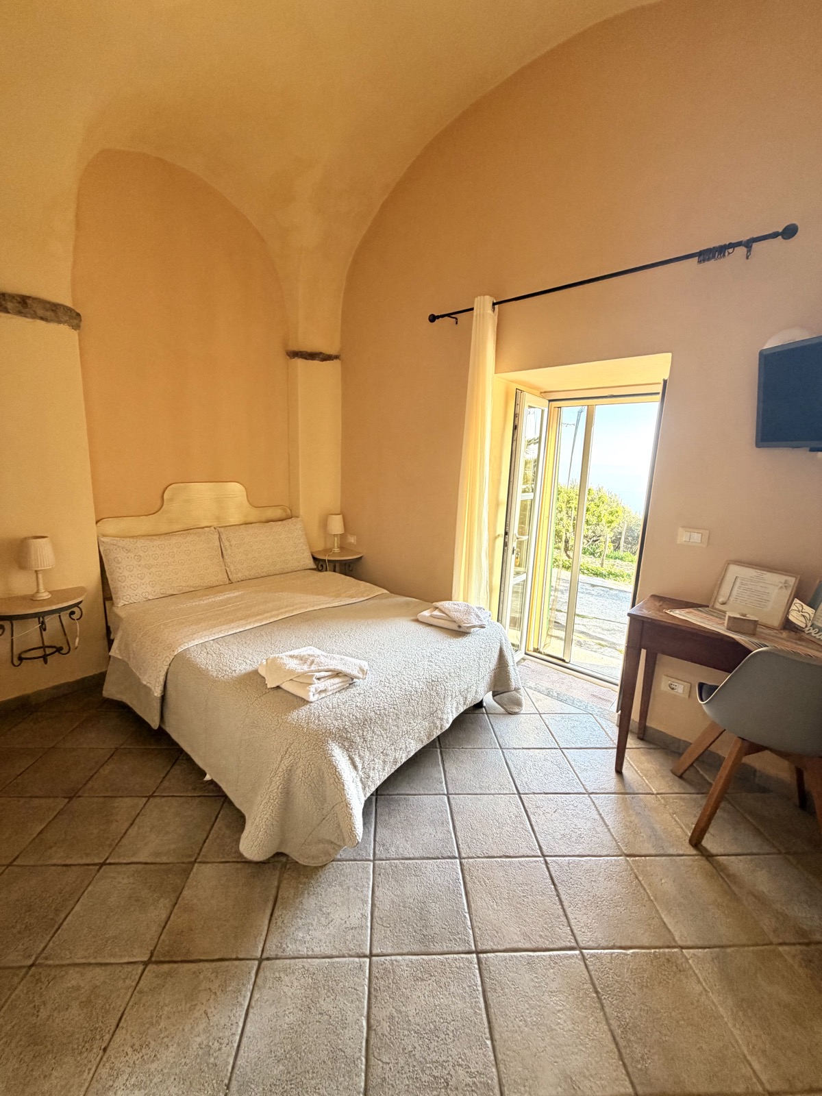 Camera Il Mare — letto matrimoniale sotto le volte a botte con porta-finestra aperta sul giardino