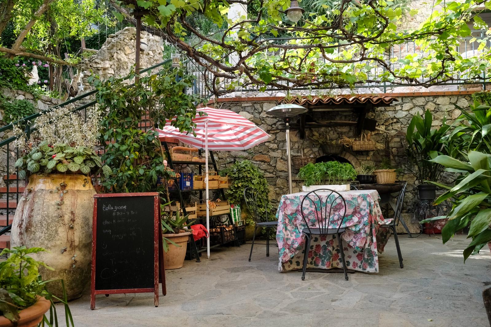 Cortile del ristorante con lavagna del menu, ombrellone e tavoli in pietra