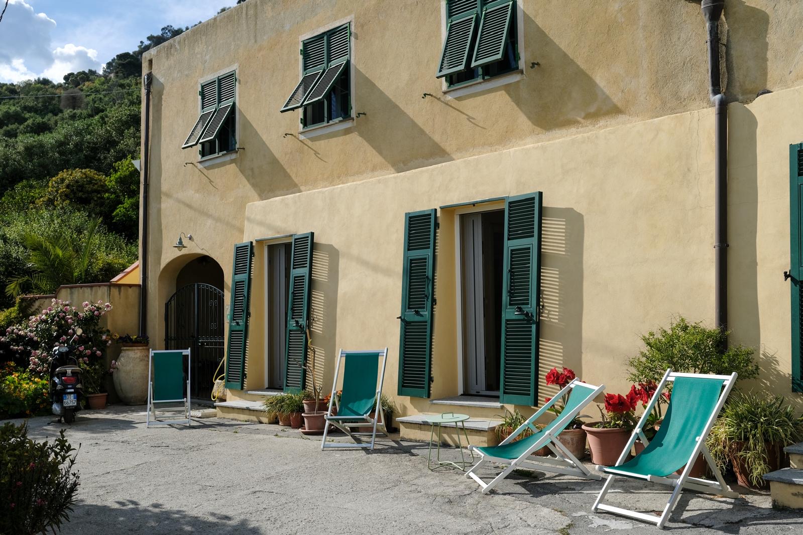 Facciata dell'agriturismo con sdraio verdi, persiane e fiori