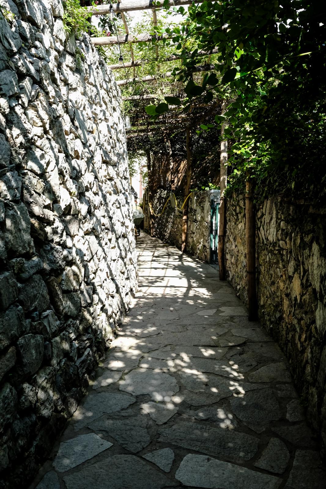 Passaggio coperto in pietra con pergolato e giochi di luce e ombra