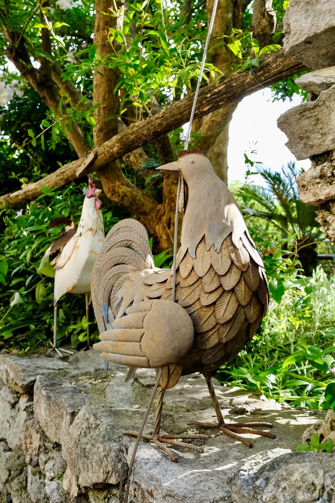 Sculture decorative di galli in metallo nel giardino tra la vegetazione